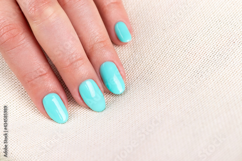 Female hand with beautiful manicure - mint blue nails on burlap fabric textile background  closeup with copy space. Selective focus