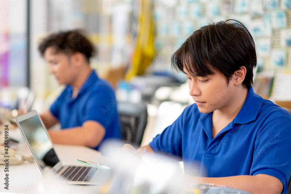 Asian garage worker or with blue uniform work in area of counter service with his co-worker and they look happy during working. Automotive part business and staff management system to support concept. Asian garage worker or with blue uniform work in area of counter service with his co-worker and they look happy during working. Automotive part business and staff management system to support concept.