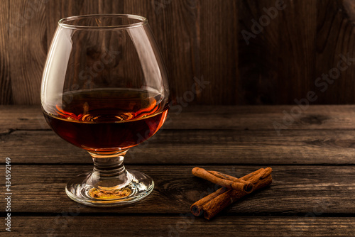 Glass of brandy with cinnamon sticks on a wooden table. Focus on the cinnamon sticks