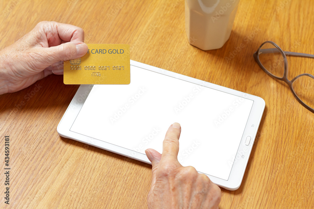 Seniors and online shopping mock up: hands of an elderly woman touching the screen of a tablet computer to pay with a credit card. Seniors and online shopping mock up: hands of an elderly woman touching the screen of a tablet computer to pay with a credit card.