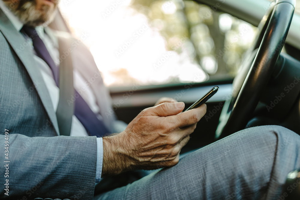 Close up photo of businessman texting on his mobile phone while driving.