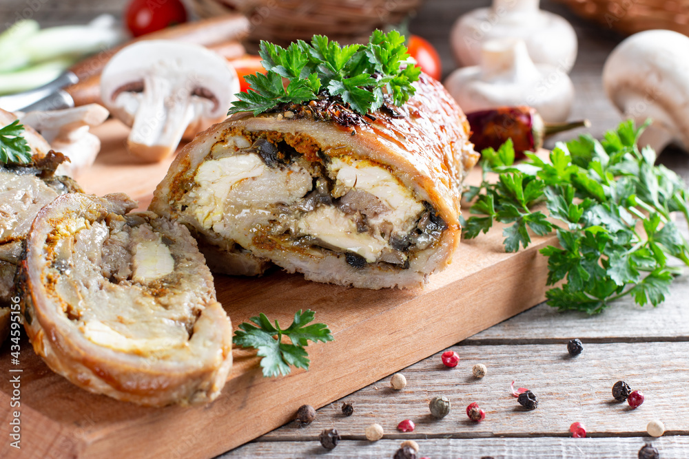 Roasted pork roll stuffed with mushrooms and cheese served with vegetables on a board Roasted pork roll stuffed with mushrooms and cheese served with vegetables on a board