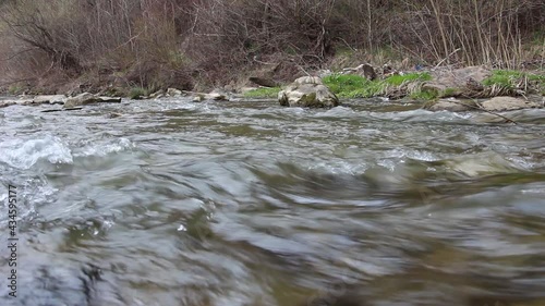 A river with cold water and stones. Fresh clean stream of water that flows in the river in springtime. A river with fresh cold water flowing in a rapid pace. The mountain river