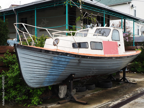 An old boat stands on an iron stand near a private house on the street