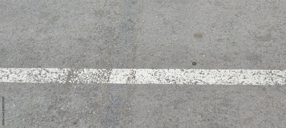 Fototapeta premium White stripe on gray asphalt. On light gray rough asphalt there is a light white stripe. The strip was applied in karsky, the paint was erased in places.