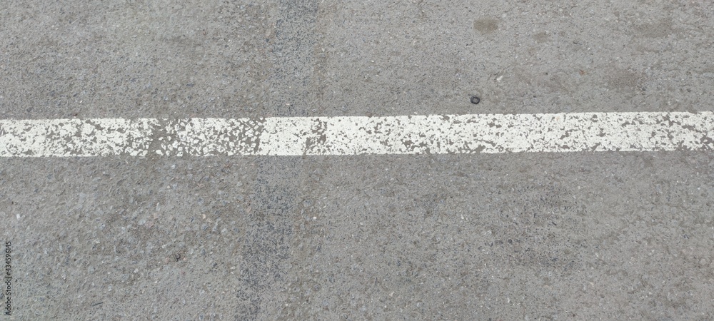 Fototapeta premium White stripe on gray asphalt. On light gray rough asphalt there is a light white stripe. The strip was applied in karsky, the paint was erased in places.