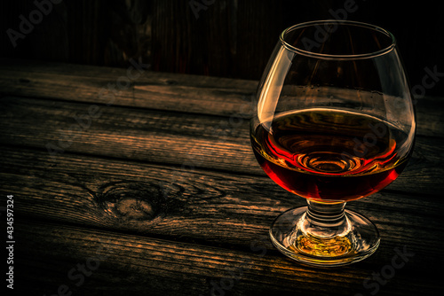 Glass of brandy and on an old wooden table. Angle view