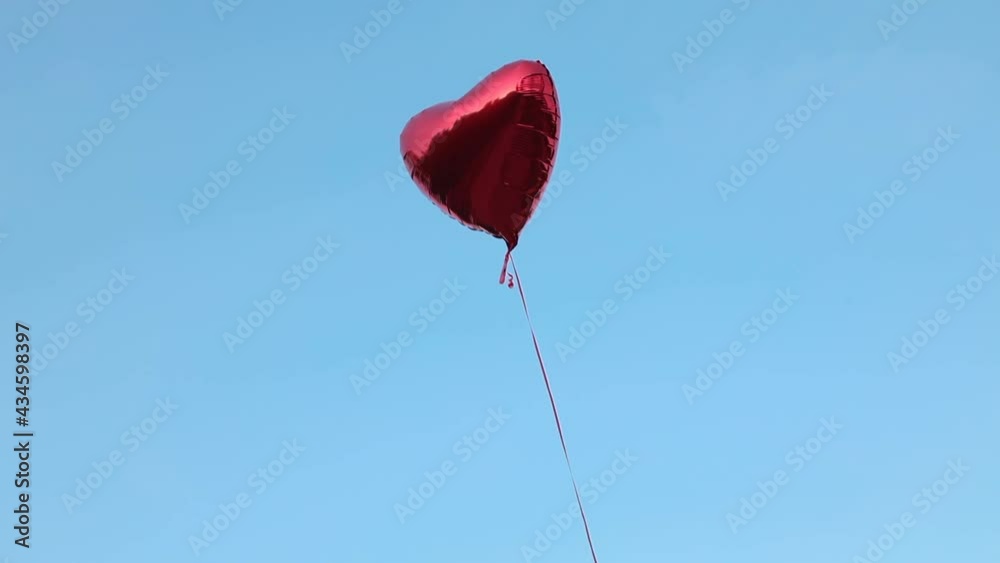 A red foil balloon in the shape of a heart filled with helium flies against the backdrop of a cloudless sky. Concept for love, Valentine's day, relationship. Full HD video footage