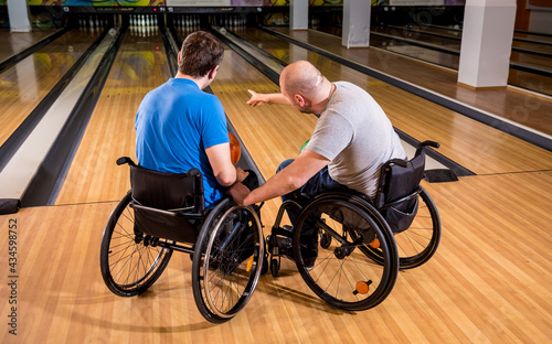 Two young disabled men in wheelchairs playing bowling in the club