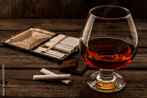 Glass of brandy and a chocolate with cigarette case on an old wooden table. Angle view