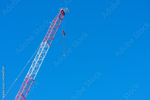 Raised jib of construction tower crane with suspended empty hook. Blue sky
