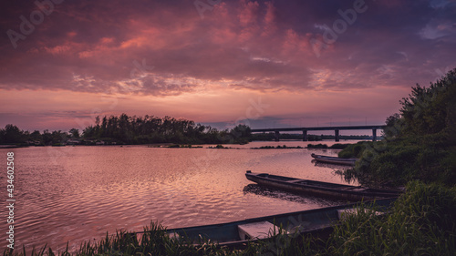 Kolorowy, różowy zachód słońca nad Wisłą, przystań z wiślanymi łódkami i most przez rzekę