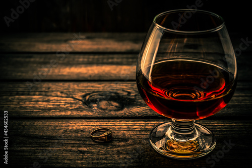 Glass of brandy and golden ring on an old wooden table. Angle view