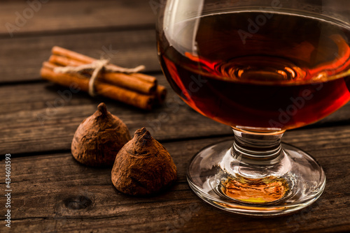 Glass of brandy and a couple of chocolate truffles with cinnamon sticks tied with jute rope on an old wooden table. Close up view, shallow depth of field