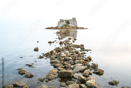 Stony path in a calm sea towards an old collapsed building. Long exposure. photo