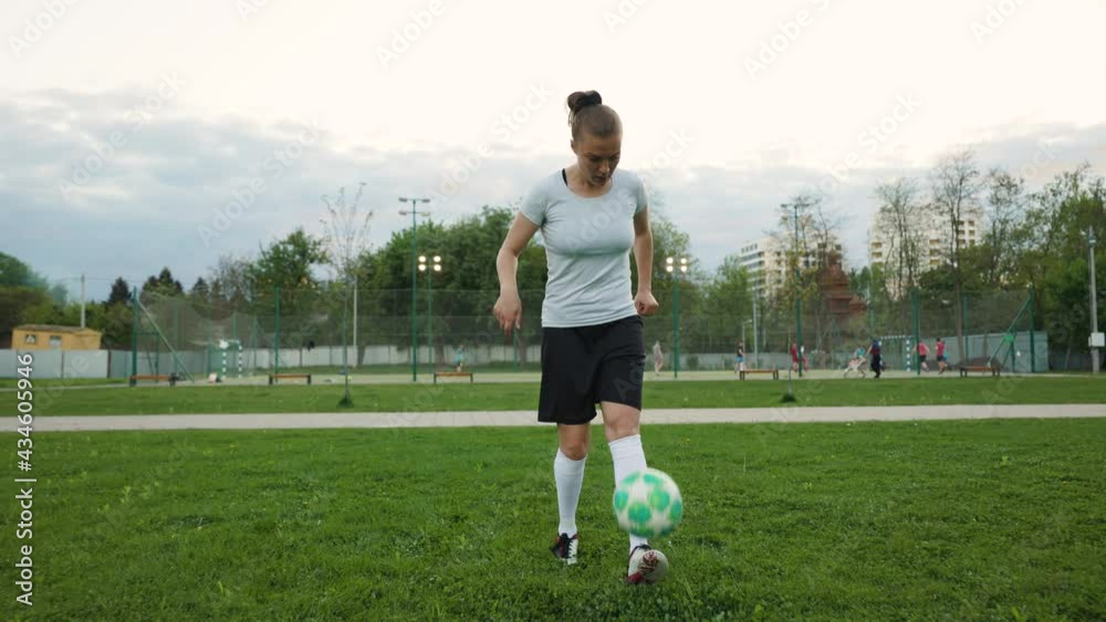 Portrait of woman football soccer player in full growth in the park. Woman in professional uniform juggling with ball. Men play football background Portrait of woman football soccer player in full growth in the park. Woman in professional uniform juggling with ball. Men play football background