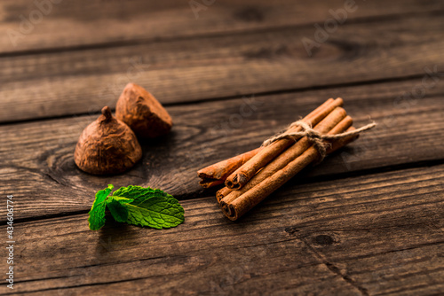 Chocolate truffles with mint sprig and cinnamon sticks tied with jute rope on an old wooden table. Close up view, shallow depth of field
