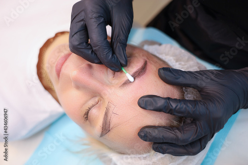 The tattoo artist wipes the newly made permanent makeup of the eyebrows with a cotton swab