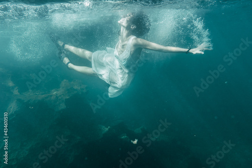 A young Caucasian brunette in a white dress jumping into the sea, underwater image, summer lifestyle