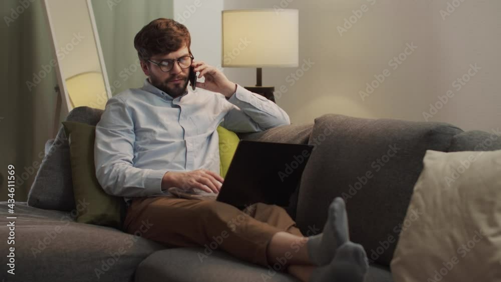 A European man is talking on the phone and working on a laptop. A European man is talking on the phone and working on a laptop.