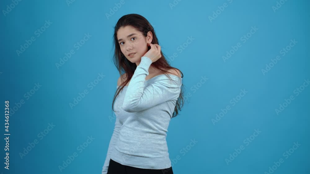 The portrait of a shy young woman who turns to one side, smiles coquettishly and puts her hair behind her ear. Asian with dark hair, dressed in a blue blouse, isolated on a dark blue background in the The portrait of a shy young woman who turns to one side, smiles coquettishly and puts her hair behind her ear. Asian with dark hair, dressed in a blue blouse, isolated on a dark blue background in the