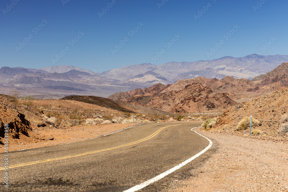 The road descends from Jubilee Pass through rocky hills toward towering mountains in southern Death Valley National Park, California

