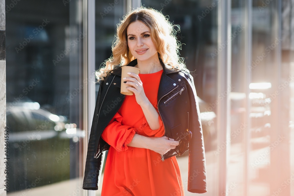 Fototapeta premium Cheerful stylish young woman in the street drinking morning coffee in sunshine light.