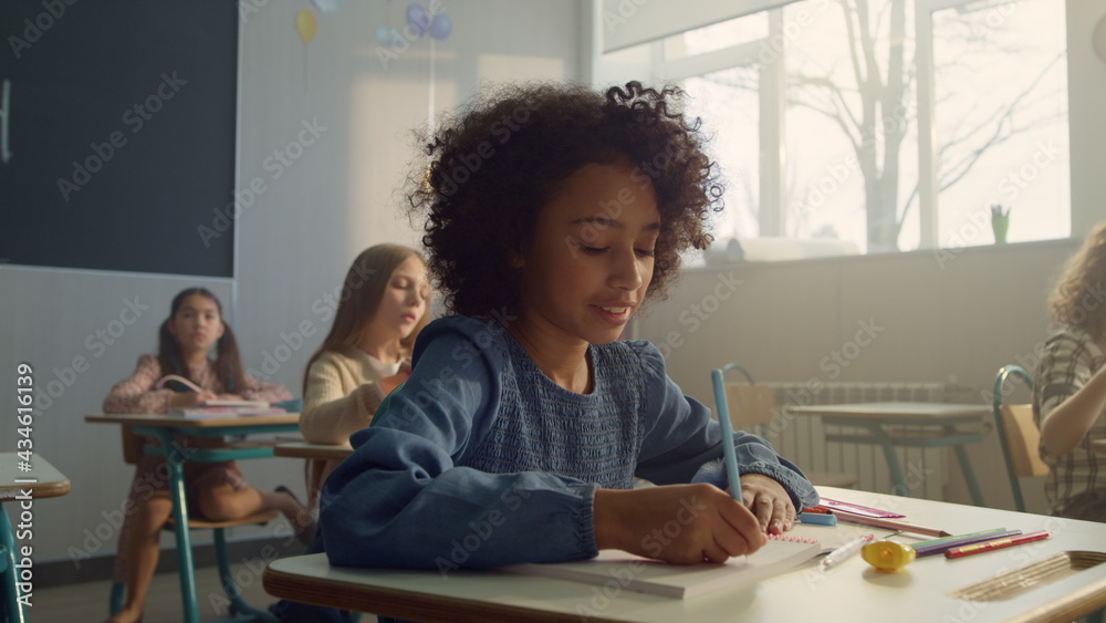 Girl sitting at desk in classroom. Cheerful student writing in notebook Girl sitting at desk in classroom. Cheerful student writing in notebook