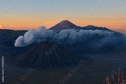 Sunset behind smoky mountain. Active volcano in clouds of smoke with crater in depth. Mount Gunung Bromo volcano in East Java, Indonesia.