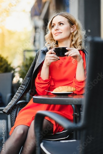 Very beautiful young woman, sit in Cafe and drink coffee or tea, street front view