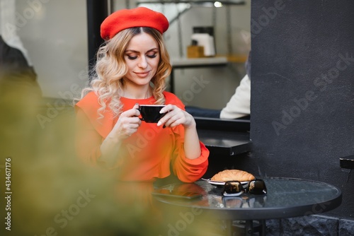 young beautifull style brunette woman with long hair dressed in red hat and dress drinking a coffee in french cafe