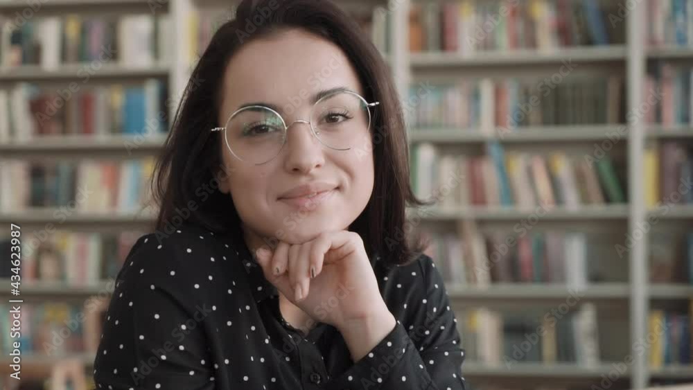 Portrait of beautiful young woman wearing glasses, bookshelf on background Portrait of beautiful young woman wearing glasses, bookshelf on background