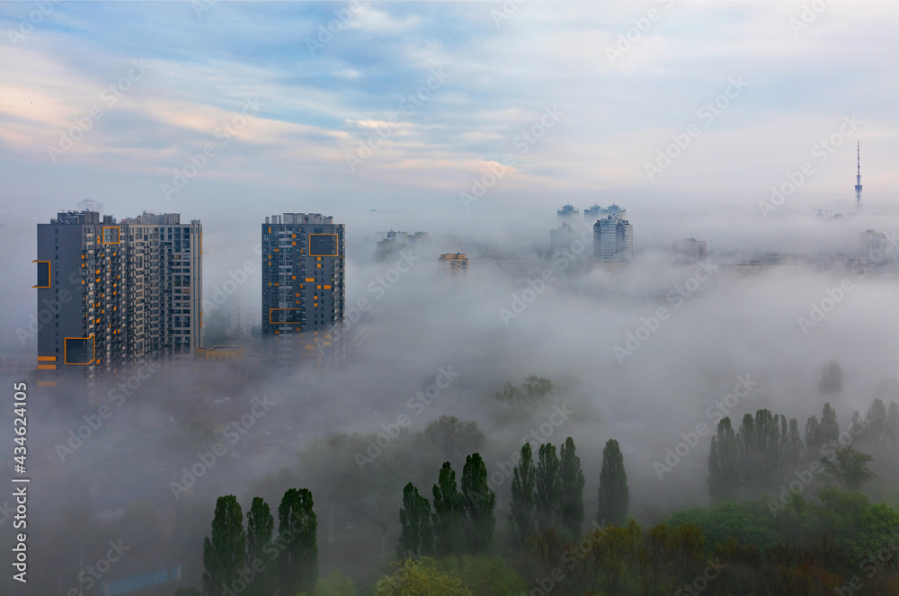 A thick fog descended in the early morning on the sleeping city and stretches between residential high-rise buildings and over the green park. A thick fog descended in the early morning on the sleeping city and stretches between residential high-rise buildings and over the green park.