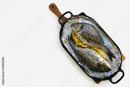 Mediterranean diet. Baked gilthead with lemon and herbs. Baked Dorada on a pan. Dorada grill. Proper nutrition. Cooked fish on a white plate with copywriting space.Dorada cooked in the oven.Baked fish photo