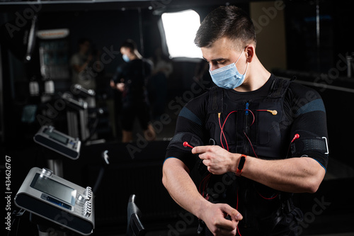 Man in EMS suit and medical mask in gym. Protection from coronavirus covid-19. Sport training in electrical muscle stimulation suit at quarantine period. photo