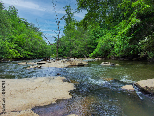 an aerial shot of the running waters of Big Creek River surrounded by miles of lush green trees and plant with rocks on the banks of the river and gorgeous sky at Vickery Creek in Roswell Georgia photo