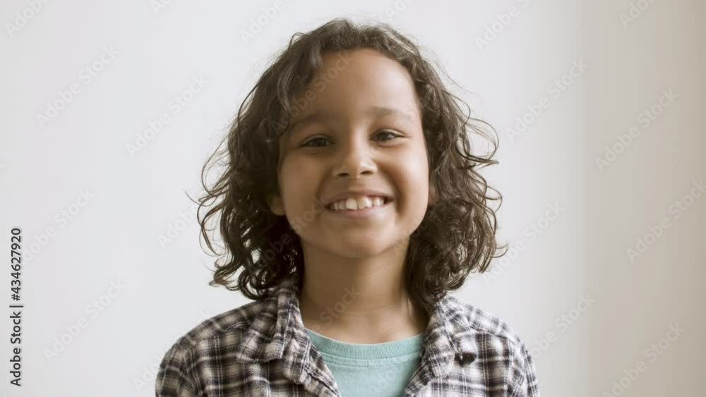 Young curly-haired boy smiling at camera. Portrait of cute Caucasian kid changing emotions on face from serious to joyful, isolated on white background. Happy boy concept. Young curly-haired boy smiling at camera. Portrait of cute Caucasian kid changing emotions on face from serious to joyful, isolated on white background. Happy boy concept.