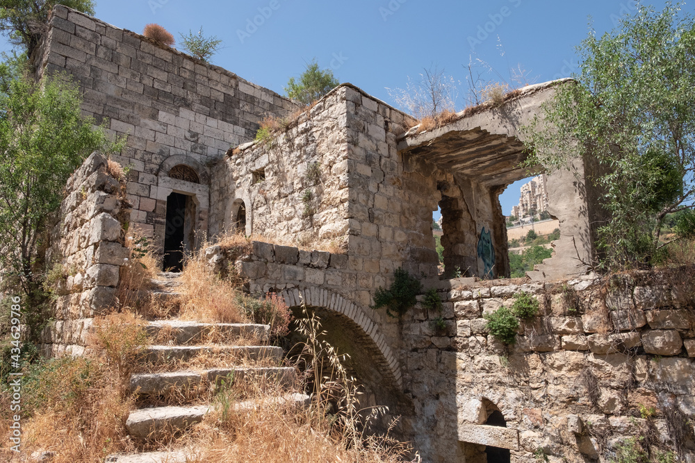 Ruins of buildings in Lifta, a depopulated Palestinian Arab village on the outskirts of Jerusalem. National nature reserve Lifta. A high-rise building of the modern Jerusalem on the background