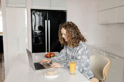 Happy woman using laptop at counter at home in the kitchen. Working from home in quarantine lockdown. Social distancing Self Isolation. High quality photo