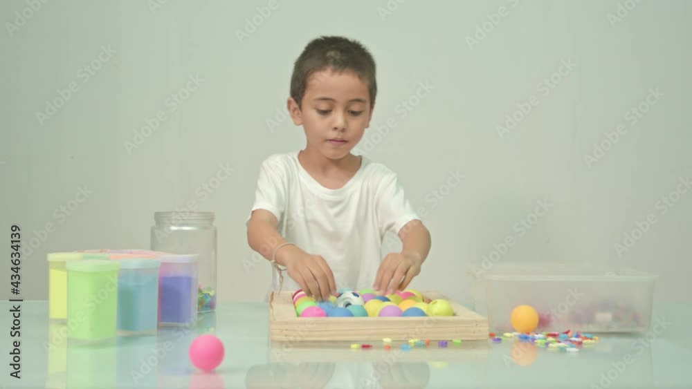The cute boy put colorful beads into a glass jar. in the white room..high quality video 4K. studio shot. The cute boy put colorful beads into a glass jar. in the white room..high quality video 4K. studio shot.