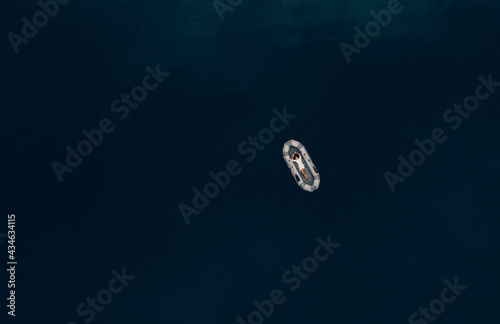 a girl in a short dress is lying on a gray inflatable boat on a blue pond top view © Olena