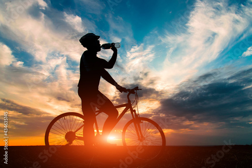 Silhouette of a cyclist drink water have a rest against the beautiful sunset.