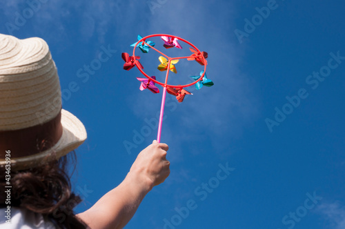 Young woman holding colorful bright rainbow toy pinwheel against blue sky photo
