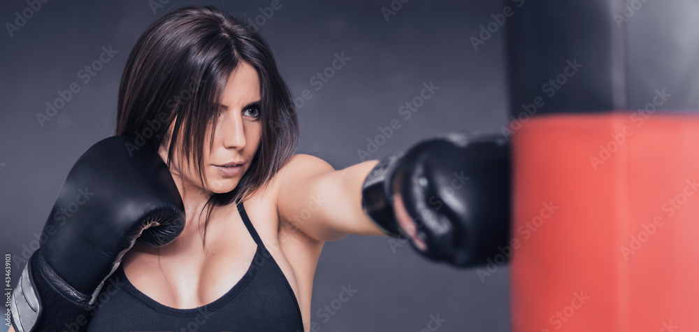 close-up of girl practicing boxing with a red bag. the boxing gloves are black. only the face is in focus. selective blur.