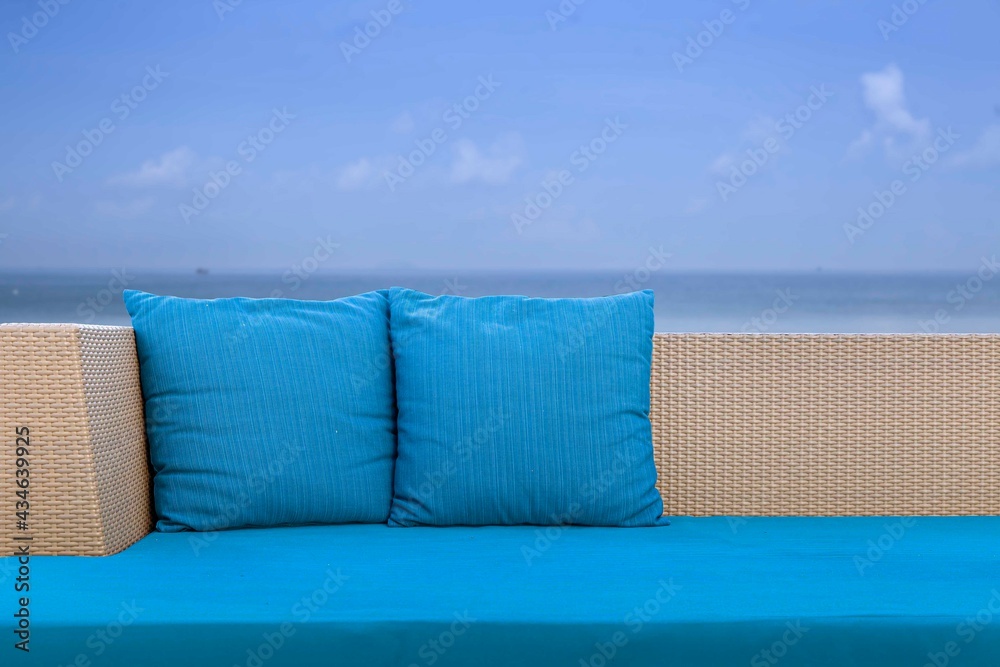 Long brown wicker sofa and blue cushions and cushions placed on the beach - obrazy, fototapety, plakaty 