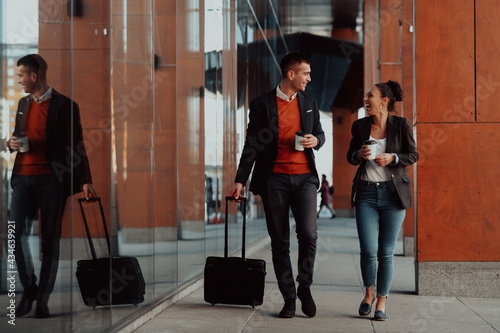 Business man and business woman talking and holding luggage traveling on a business trip, carrying fresh coffee in their hands.Business concept