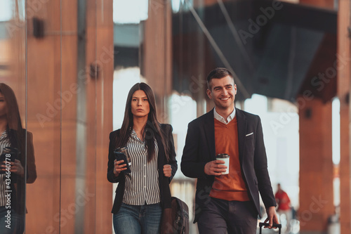 Business man and business woman talking and holding luggage traveling on a business trip, carrying fresh coffee in their hands.Business concept © .shock