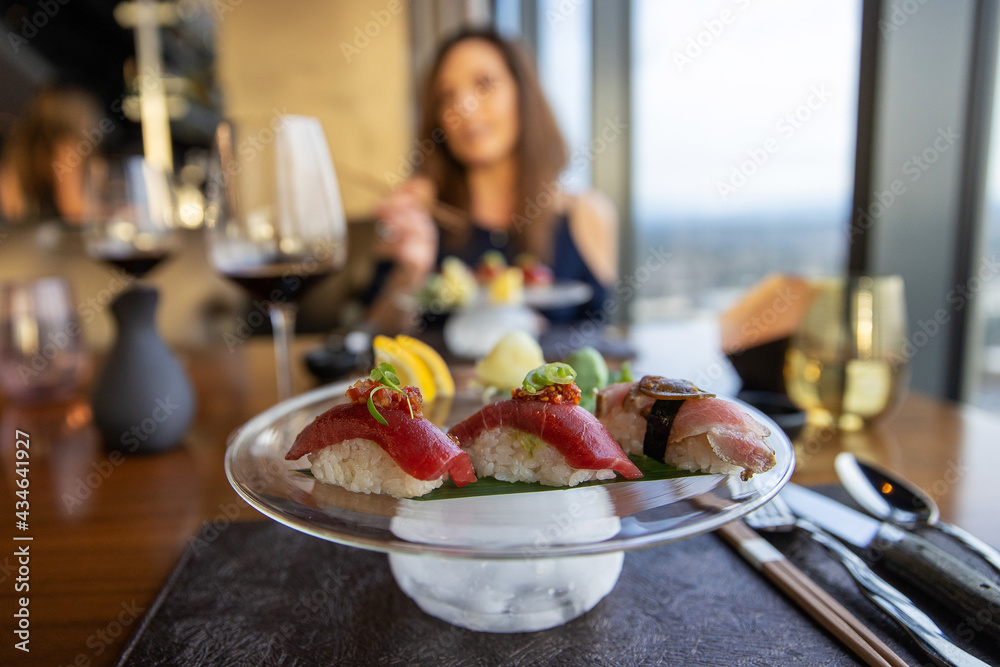 Fresh Bluefin Tuna Sushi Nigiri on a plate. A woman sits at the table with red wine on a date. 