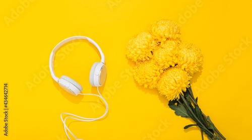 Fototapeta Naklejka Na Ścianę i Meble -  Large white headphones and lush chrysanthemum flower on yellow background with space for text. A gentle and romantic melody. Hello Spring. Flower shop. Musical accessories store. Summertime lifestyle