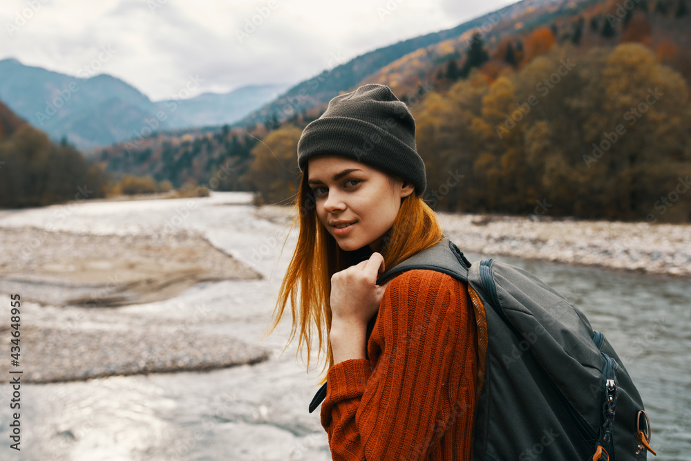 woman in a sweater cap with a backpack on her back mountain river in nature